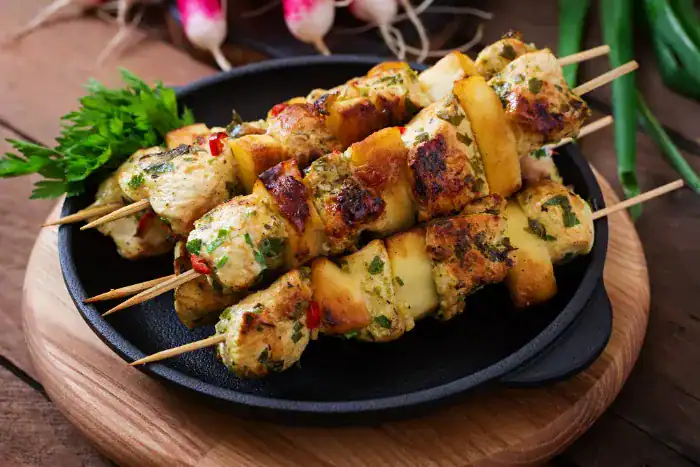 Grilled chicken kebabs with herbs and potatoes on skewers, served in a black pan