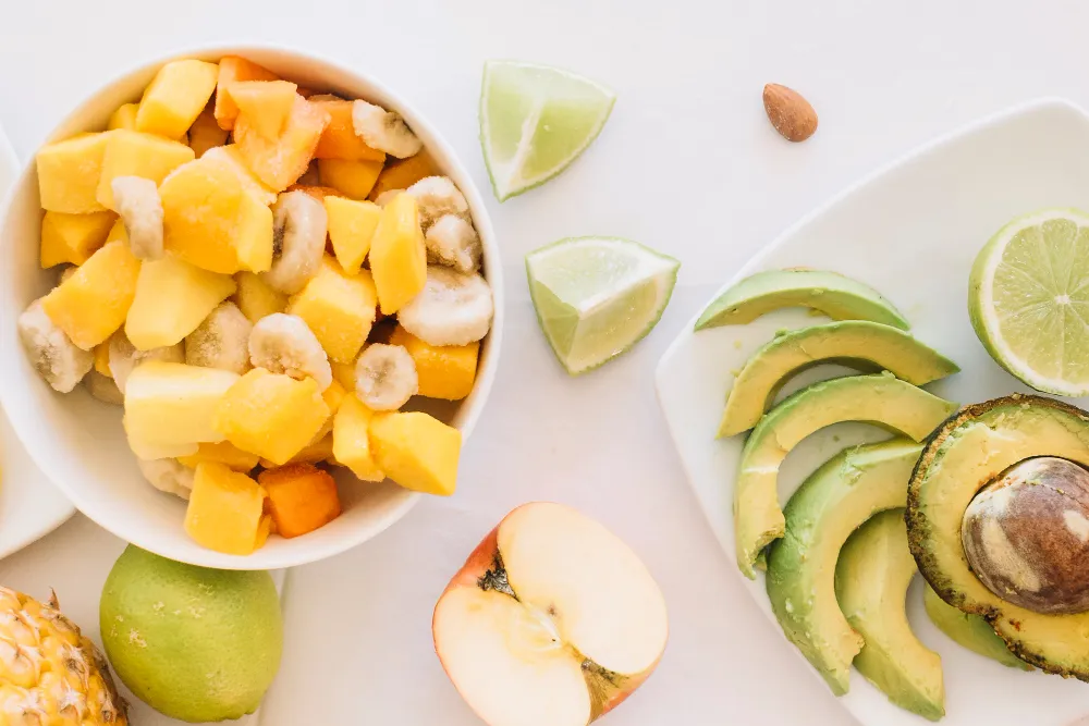Bowl of mixed tropical fruits and sliced avocado with lime wedges