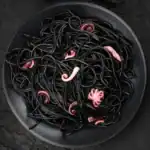 Black squid ink spaghetti with baby octopus tentacles served in a dark bowl