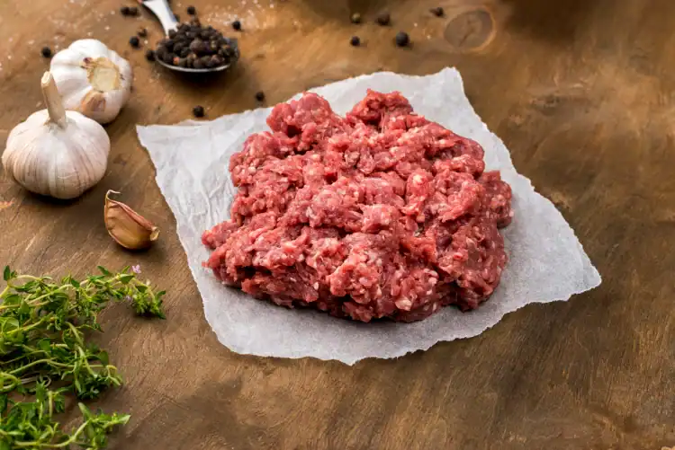 Fresh ground meat on parchment paper with garlic, peppercorns, and herbs – perfect for homemade seekh kebabs.