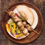 Chicken kebab skewers served in pita bread with fresh lettuce, peppers, and onions on a wooden board