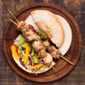 Grilled chicken kebabs served in pita bread with colorful salad on a wooden plate