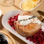 Grilled tuna steak topped with creamy sauce, served on pomegranate seeds, garnished with herbs