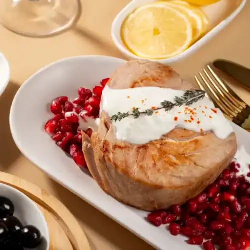Grilled tuna steak topped with creamy sauce, served on pomegranate seeds, garnished with herbs