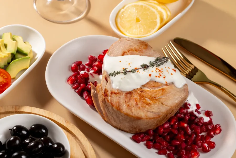 Grilled tuna steak topped with creamy sauce, served on pomegranate seeds, garnished with herbs