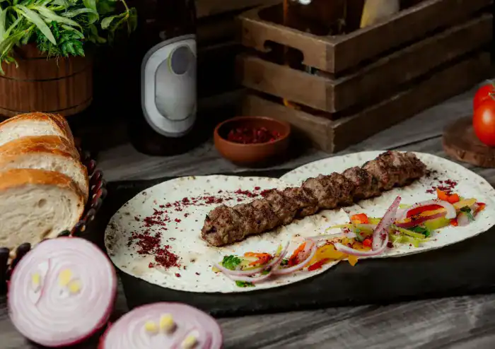 Adana kebab served on flatbread with grilled vegetables and sumac onions