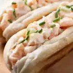 Close-up of a creamy lobster roll with fresh chives in a toasted split-top bun.
