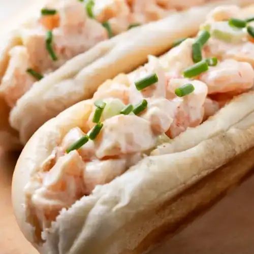 Close-up of a creamy lobster roll with fresh chives in a toasted split-top bun.