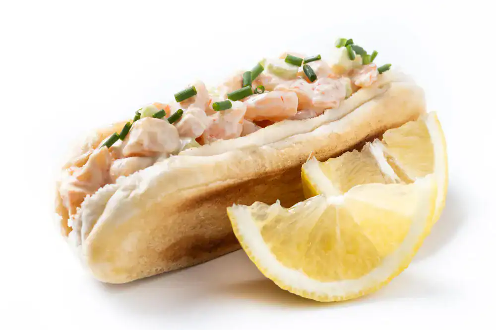 Homemade lobster roll with creamy filling and fresh chives, served with lemon wedges on the side.
