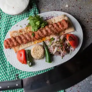 Authentic Adana kebab served on lavash with bulgur, grilled vegetables, sumac onions, and fresh parsley
