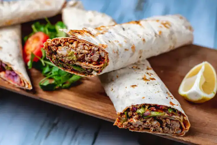 Grilled doner kebab wraps filled with meat, vegetables, and herbs served on a wooden board