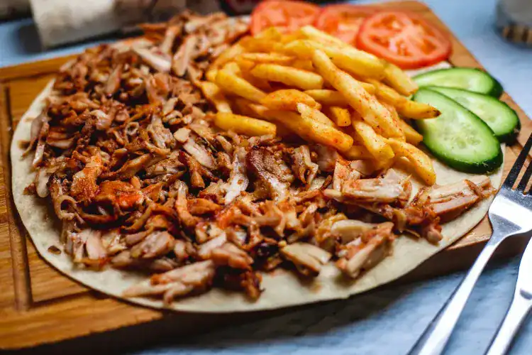 Doner kebab plate with sliced meat, spiced fries, tomatoes, and cucumber on flatbread