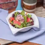 Fresh tuna salad with mixed greens, red onion rings, grapefruit slices, and basil in a white bowl
