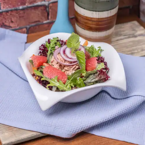Fresh tuna salad with mixed greens, red onion rings, grapefruit slices, and basil in a white bowl