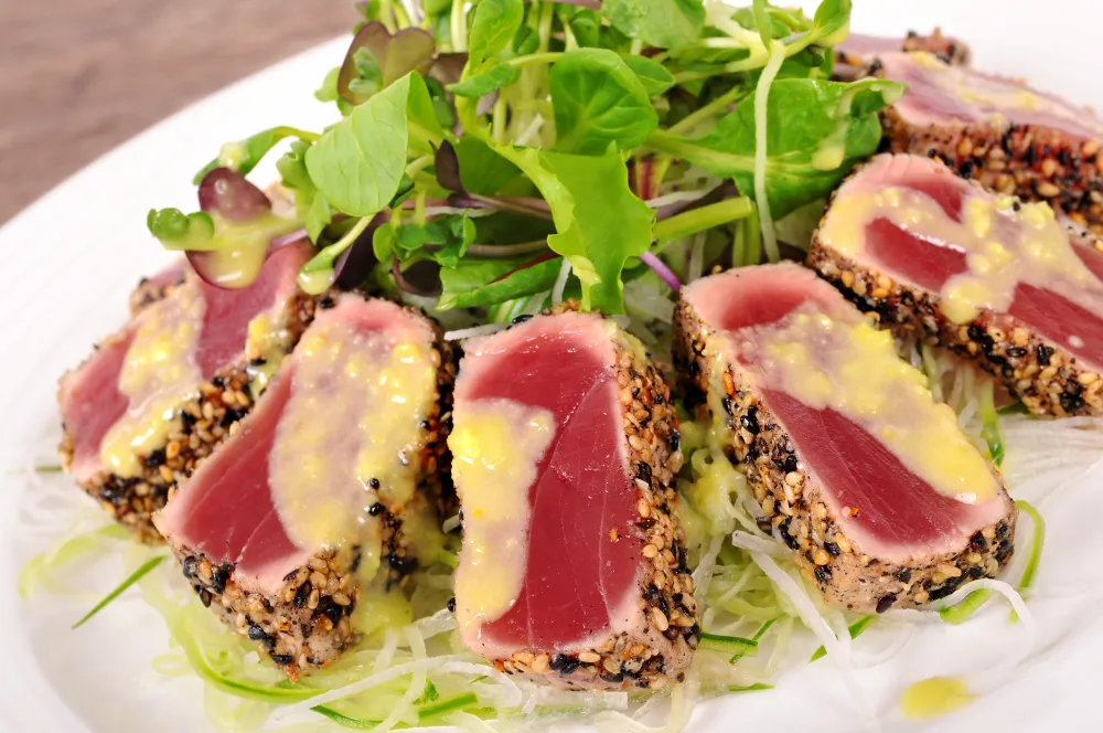 Seared sesame-crusted tuna steak slices with mustard sauce and fresh salad greens
