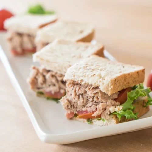 Tuna sandwich with lettuce and tomato on whole grain bread, served on a white rectangular plate
