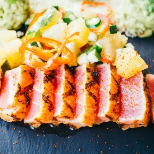 Sliced pan-seared tuna steak with pineapple salsa and guacamole on a slate plate