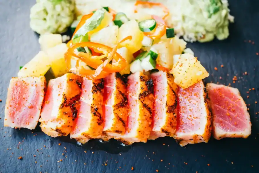 Sliced pan-seared tuna steak with pineapple salsa and guacamole on a slate plate