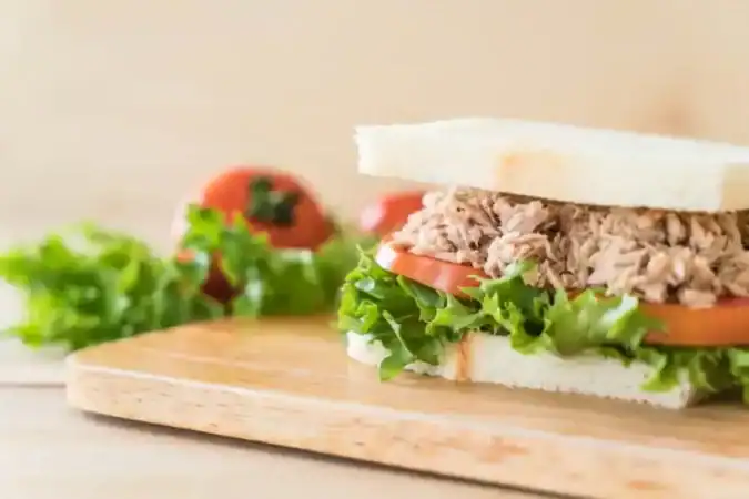 Fresh tuna sandwich with lettuce and tomato on white bread, placed on a wooden board