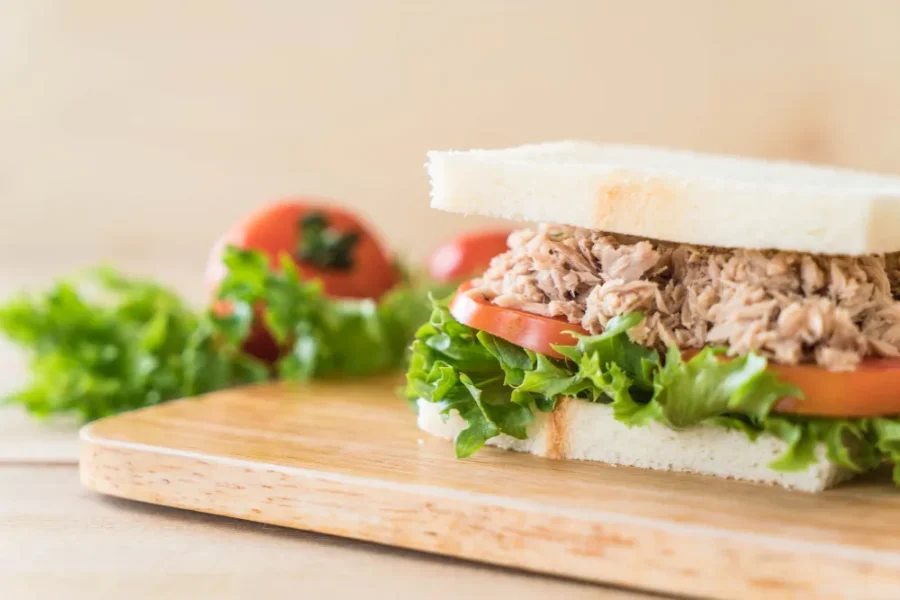Fresh tuna sandwich with lettuce and tomato on white bread, placed on a wooden board