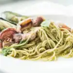 Spaghetti with squid tentacles, mussels, and pesto sauce on a white plate
