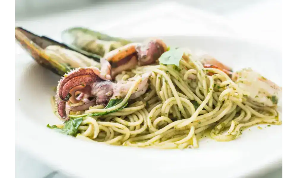 Spaghetti with squid tentacles, mussels, and pesto sauce on a white plate