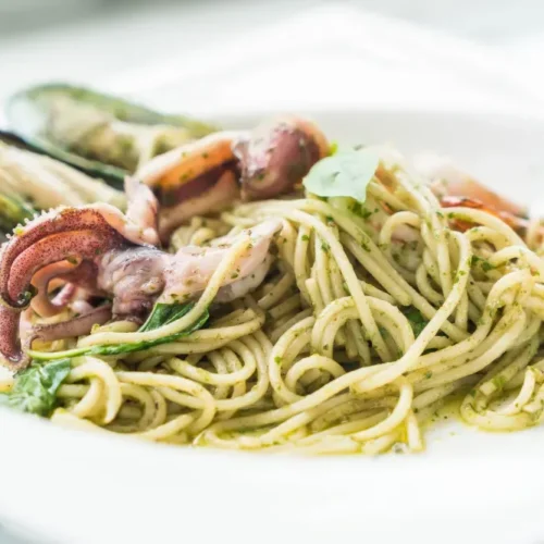 Spaghetti with squid tentacles, mussels, and pesto sauce on a white plate