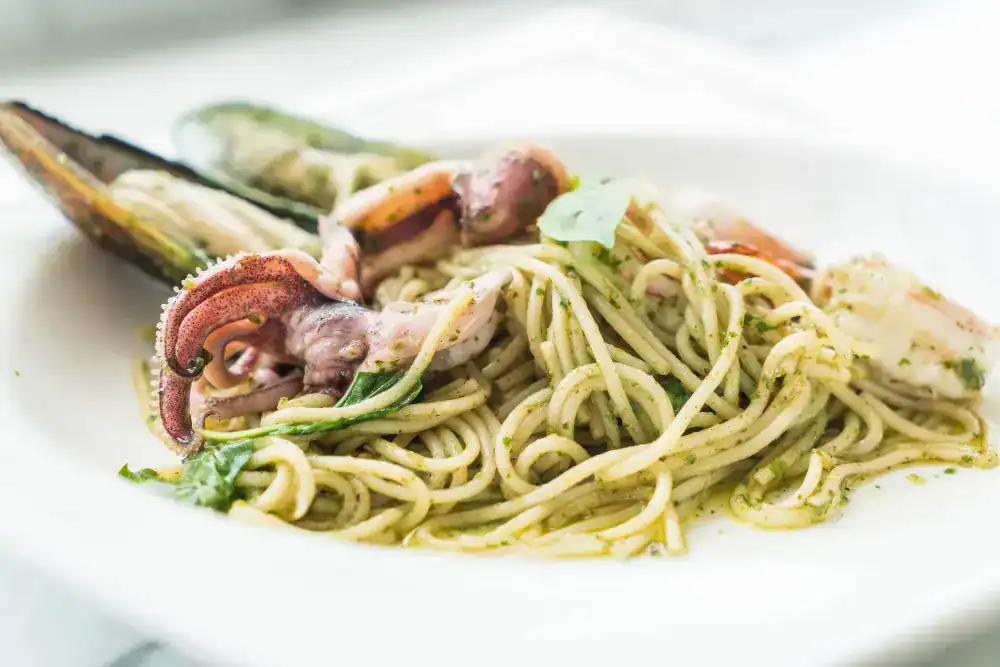 Spaghetti with squid tentacles, mussels, and pesto sauce on a white plate