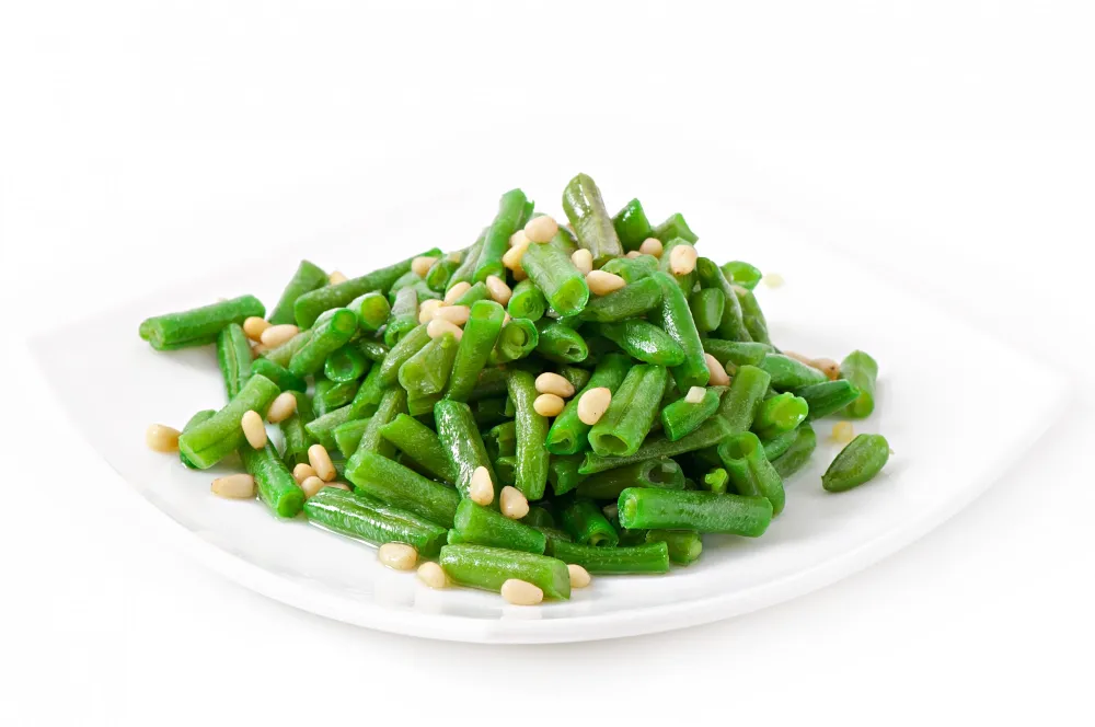 Sautéed green beans with pine nuts on a white plate