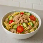 Creamy tuna pasta salad in a white bowl with cherry tomatoes, cucumber, corn, and rotini pasta