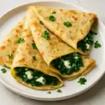 Close-up of spinach and cheese crepes folded on a white plate and garnished with fresh parsley.
