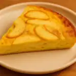 Single slice of apple frittata on a white plate with warm golden tones