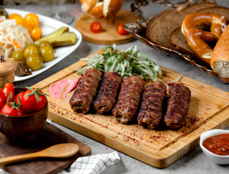 Grilled kofta kebabs on skewers served with fresh tomatoes, lemon, and mixed vegetable salad
