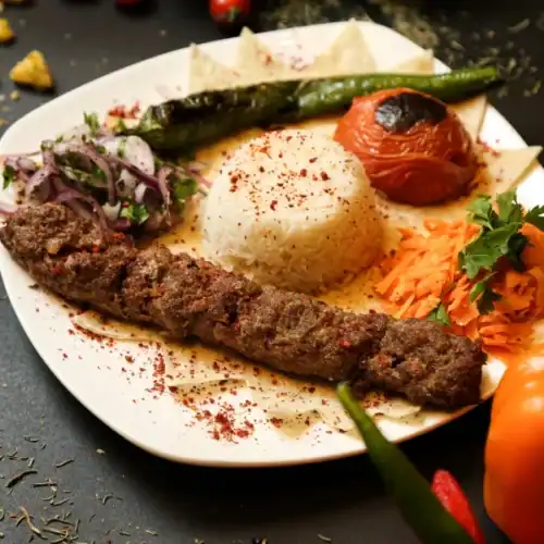 Juicy kofta kebab plate served with rice, grilled tomato, green pepper, and fresh vegetables