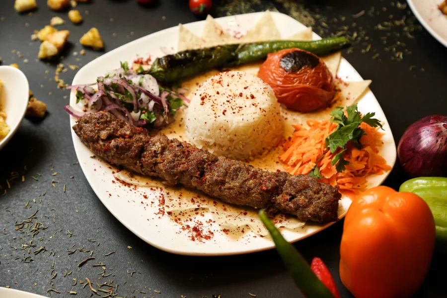 Juicy kofta kebab plate served with rice, grilled tomato, green pepper, and fresh vegetables
