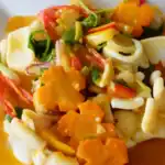 Colorful stir-fried squid dish with vegetables and carrot flowers on a white plate.