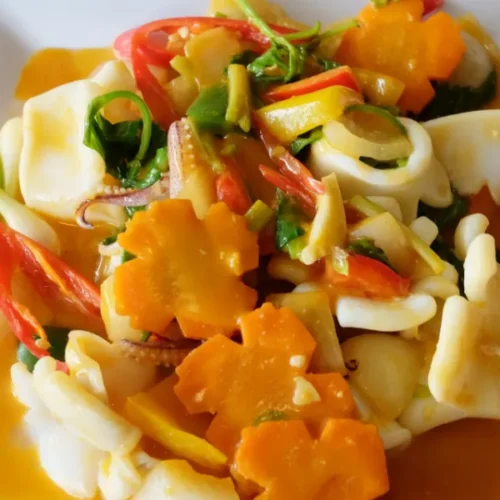Colorful stir-fried squid dish with vegetables and carrot flowers on a white plate.