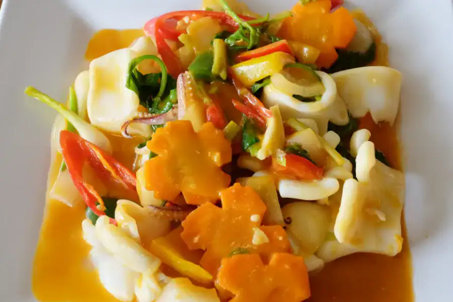 Colorful stir-fried squid dish with vegetables and carrot flowers on a white plate.
