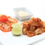Fried calamari served with lime, tomato salad, and dipping sauce on a white plate.