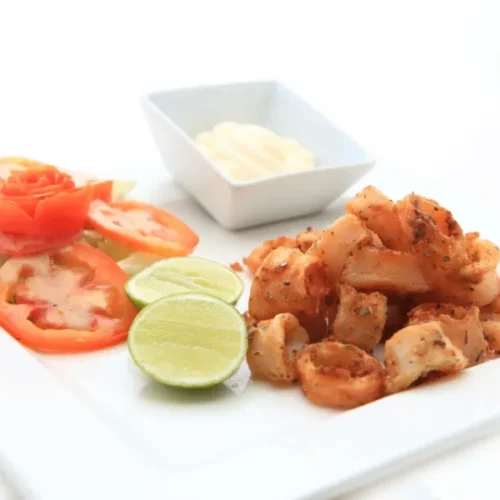 Fried calamari served with lime, tomato salad, and dipping sauce on a white plate.