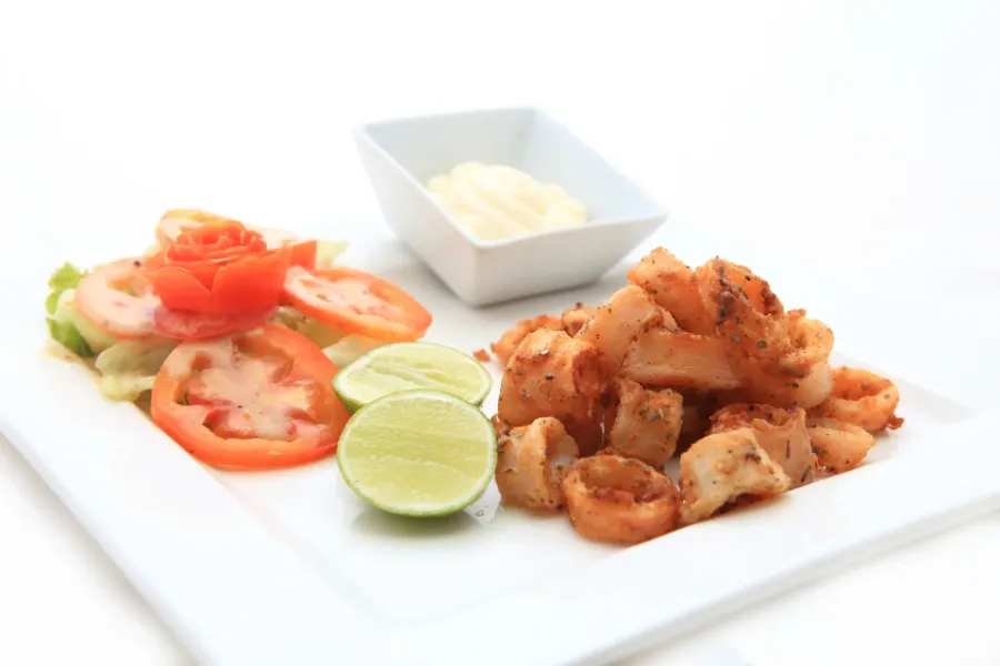 Fried calamari served with lime, tomato salad, and dipping sauce on a white plate.