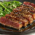 Seared tuna steak sliced and topped with sesame seeds, served with mixed greens and soy glaze.