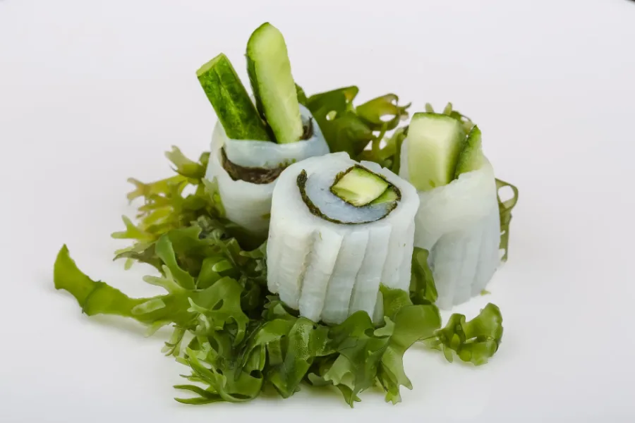 Squid sashimi rolls filled with cucumber, served on a bed of green seaweed