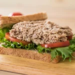 Open tuna sandwich on whole grain bread with lettuce and tomato on a wooden board