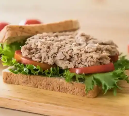 Open tuna sandwich on whole grain bread with lettuce and tomato on a wooden board