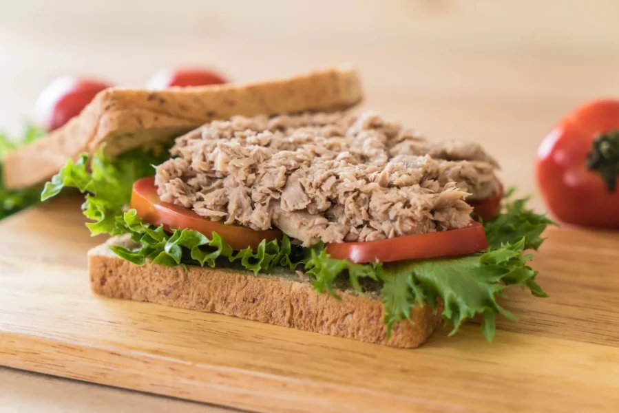 Open tuna sandwich on whole grain bread with lettuce and tomato on a wooden board