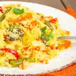 Colorful couscous dish with mixed vegetables served on a white plate with a fork.