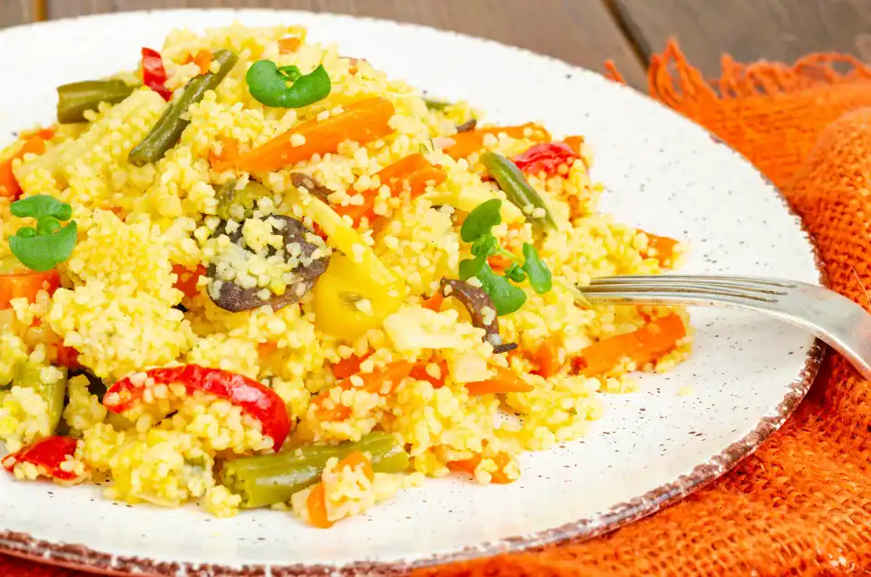 Colorful couscous dish with mixed vegetables served on a white plate with a fork.