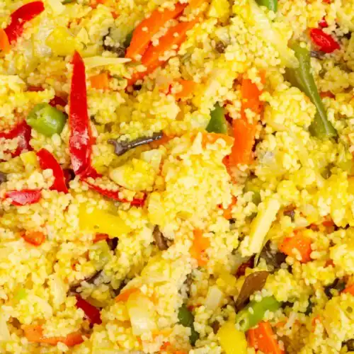 Close-up of couscous mixed with colorful vegetables including carrots, peppers, and green beans.