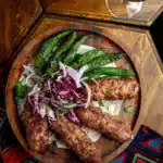 Grilled kofta kebabs served with roasted green peppers and sumac onions on a wooden platter